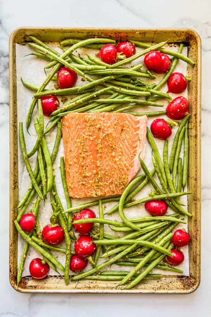 A sheet pan with an uncooked piece of salmon, green beans, and radishes.