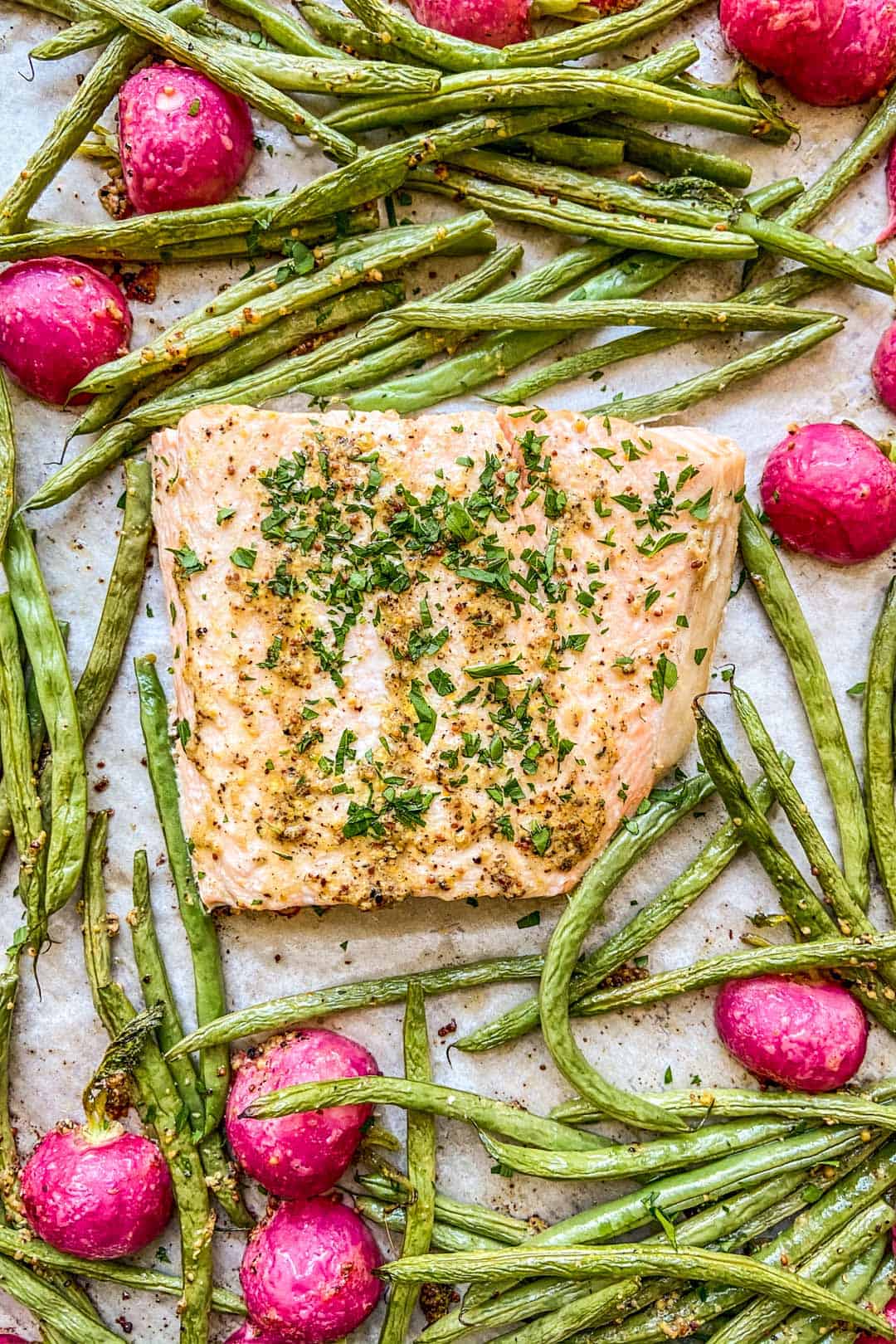 A closeup shot of a cooked salmon fillet surrounded by green beans and radishes.