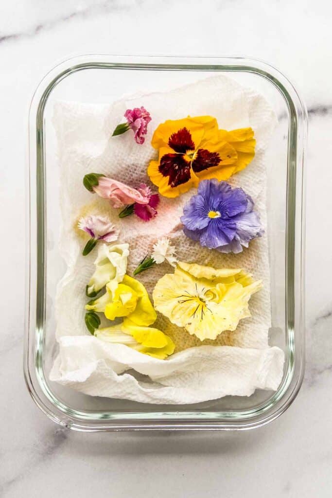 Edible flowers on a paper towel in a glass container.