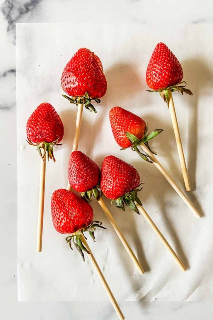 Strawberries on skewers on a piece of parchment paper.