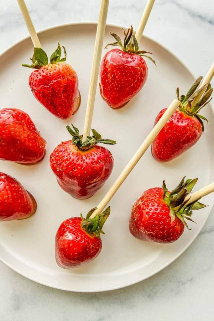 Candied strawberries on skewers sitting on a white plate.