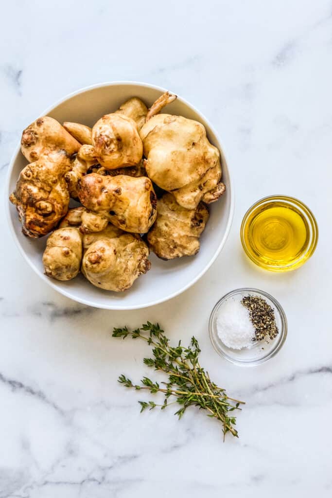 A bowl of sunchokes, a bowl of olive oil, a bowl with salt and pepper, and some fresh thyme.