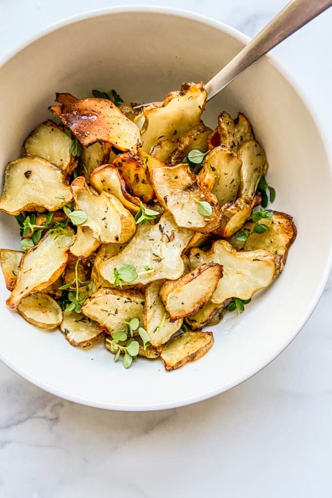 A bowl of roasted sunchokes with a silver spoon.