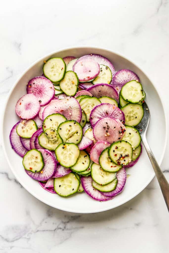 A bowl of sliced purple daikon radishes and English cucumber, topped with a sesame dressing.