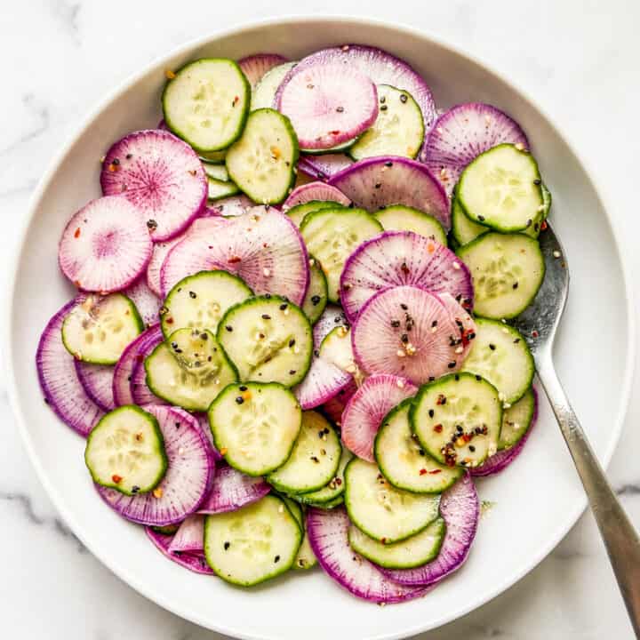 A bowl of sliced purple daikon radishes and English cucumber, topped with a sesame dressing.