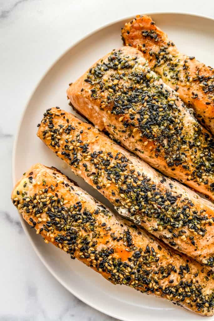 Four cooked salmon fillets topped with furikake seasoning on a white plate.