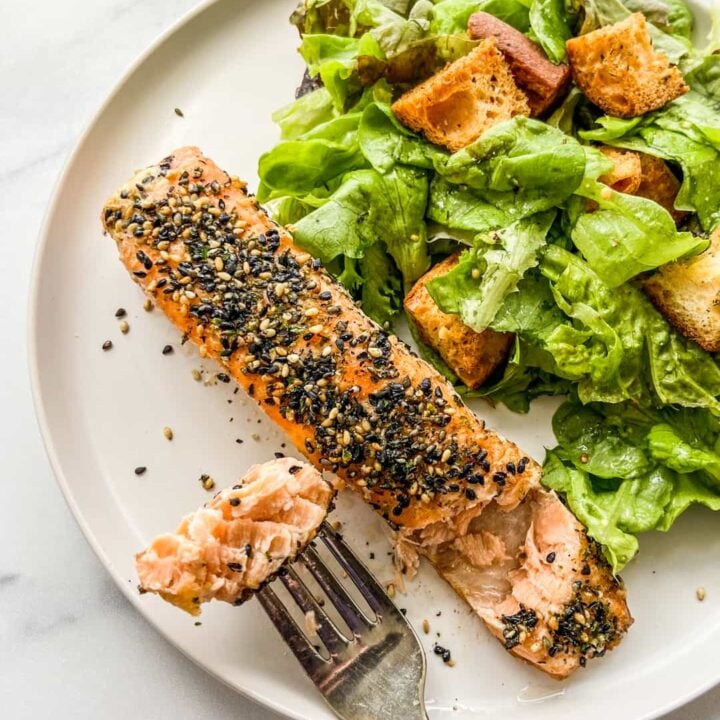 A salmon fillet topped with furikake next to a green salad on a white plate.