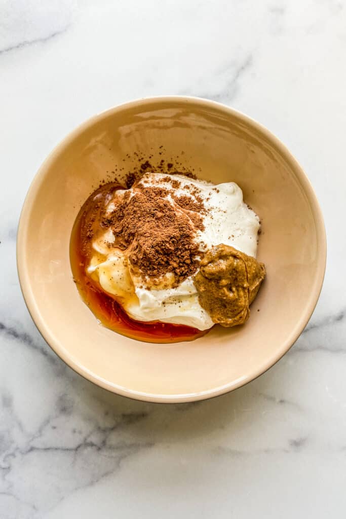 An overhead shot of a bowl with yogurt, honey, cocoa powder, and almond butter. 