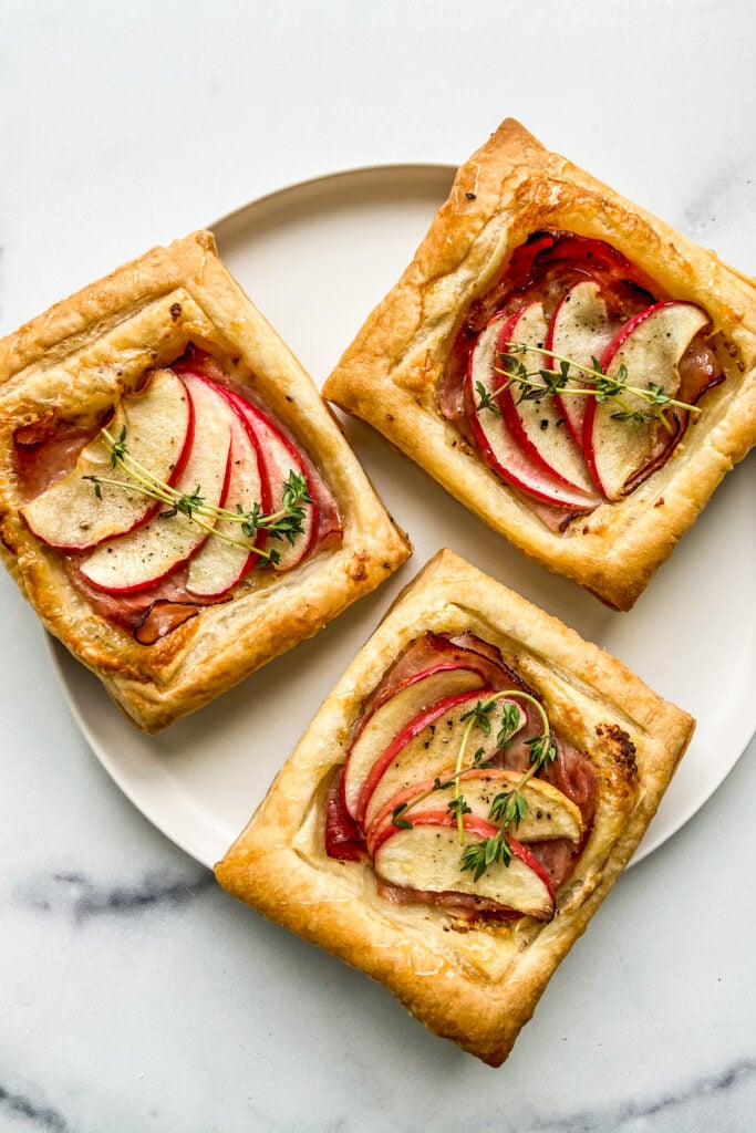 Three ham and cheese tarts on a white plate.