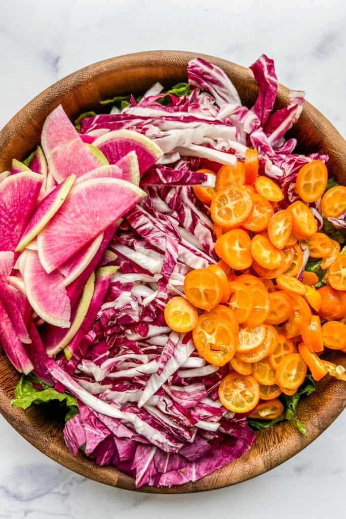 A salad bowl with shredded radicchio, sliced watermelon radish, and slices kumquats.