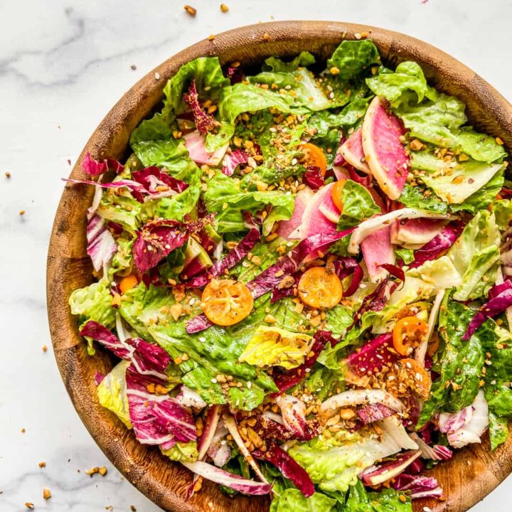 A large wooden salad bowl with a greens, radicchio, kumquats, and watermelon radishes.