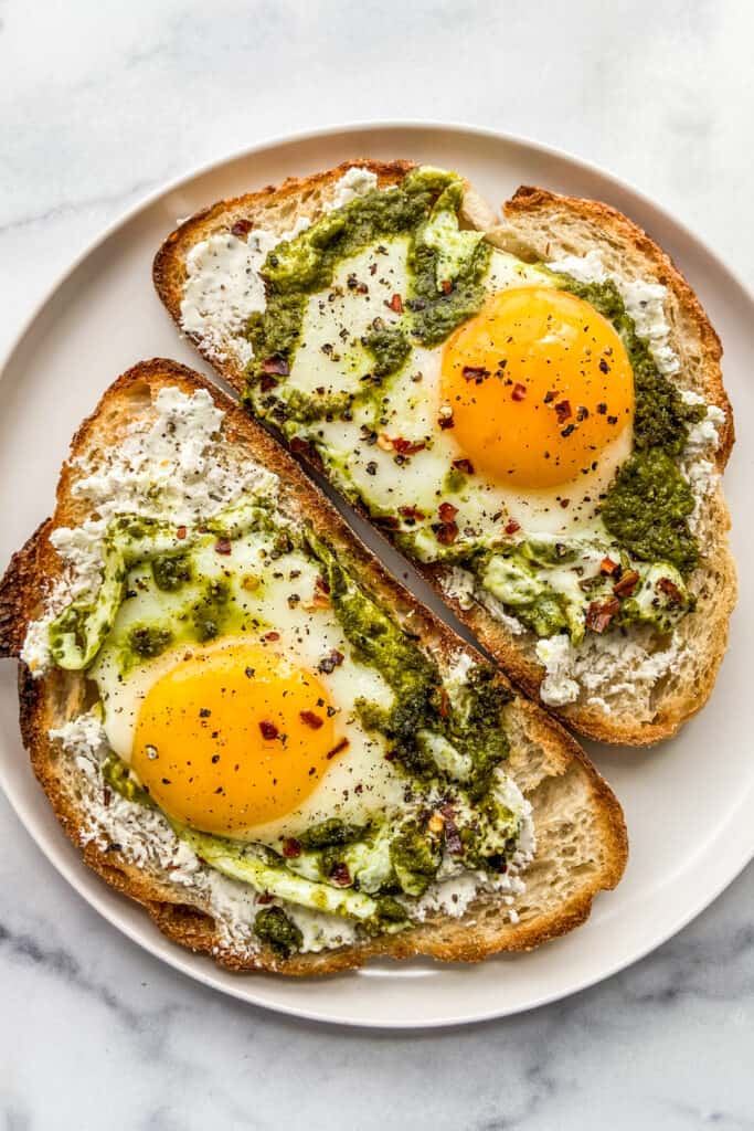 Two pieces of toast with pesto eggs on them. 