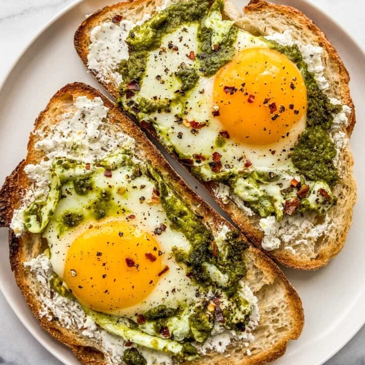 Two pieces of toast with pesto eggs on them.