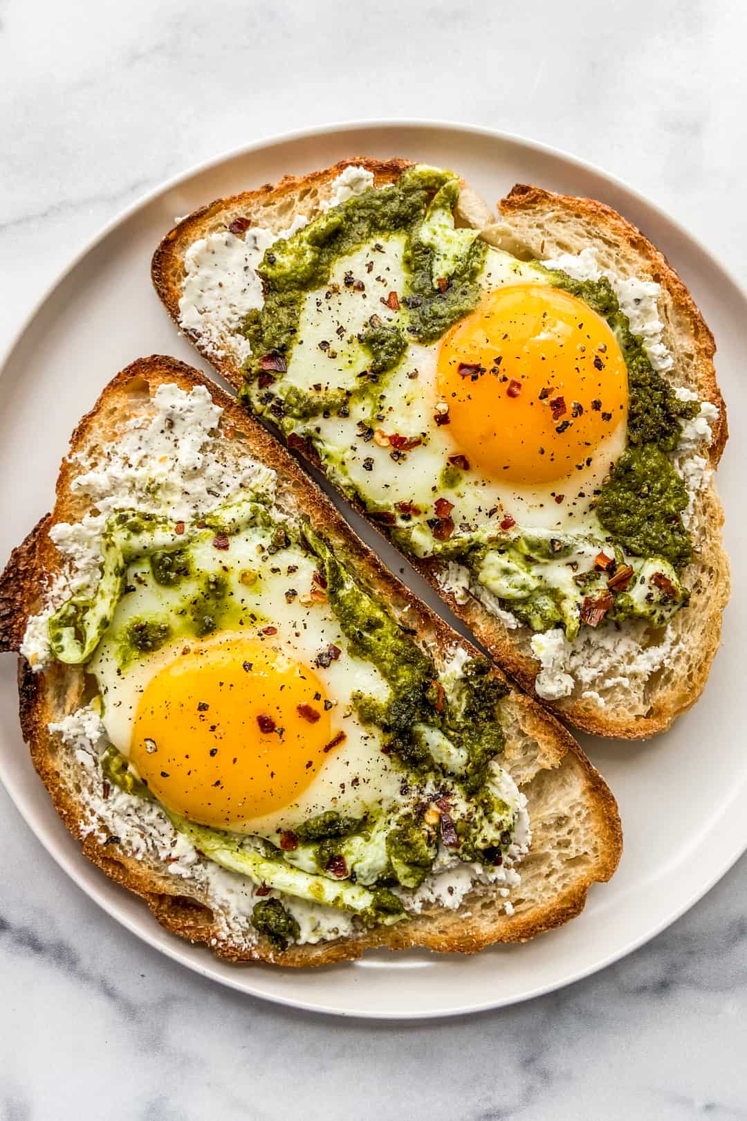 Two pieces of toast with pesto eggs on them.