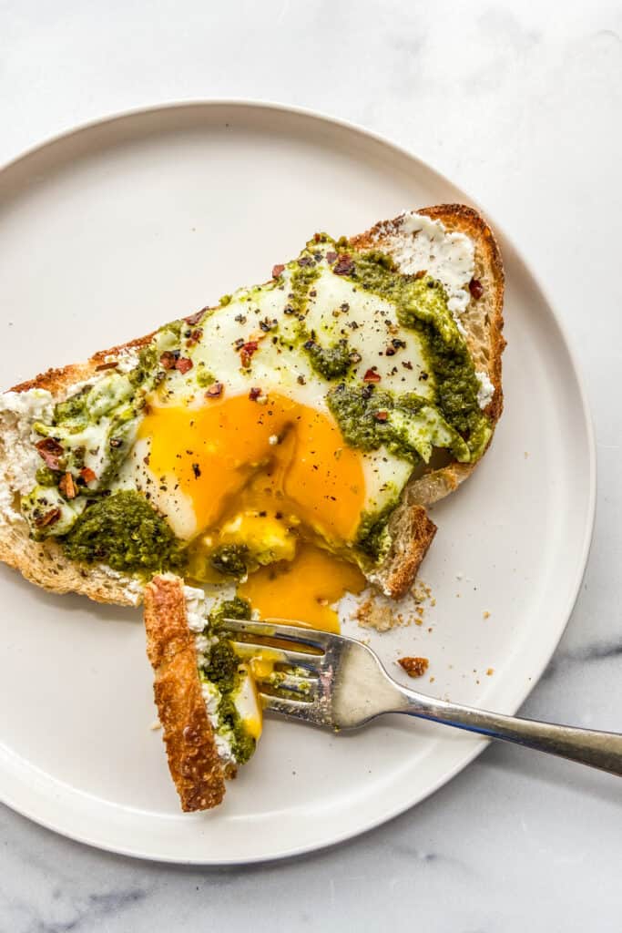 Pesto eggs on toast on a white plate with a fork.