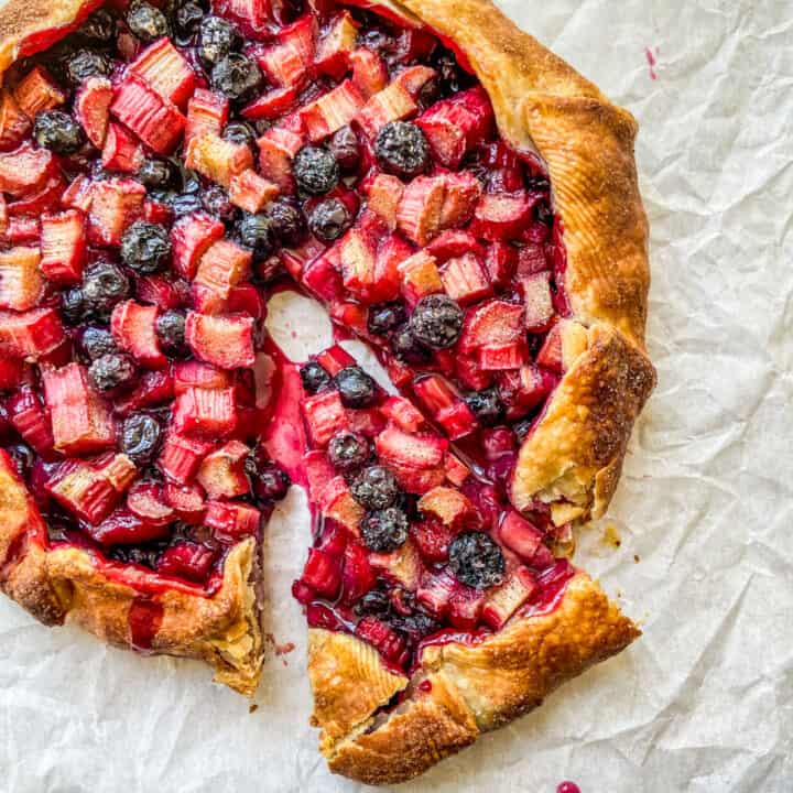 A rhubarb blueberry galette with a piece cut from it.