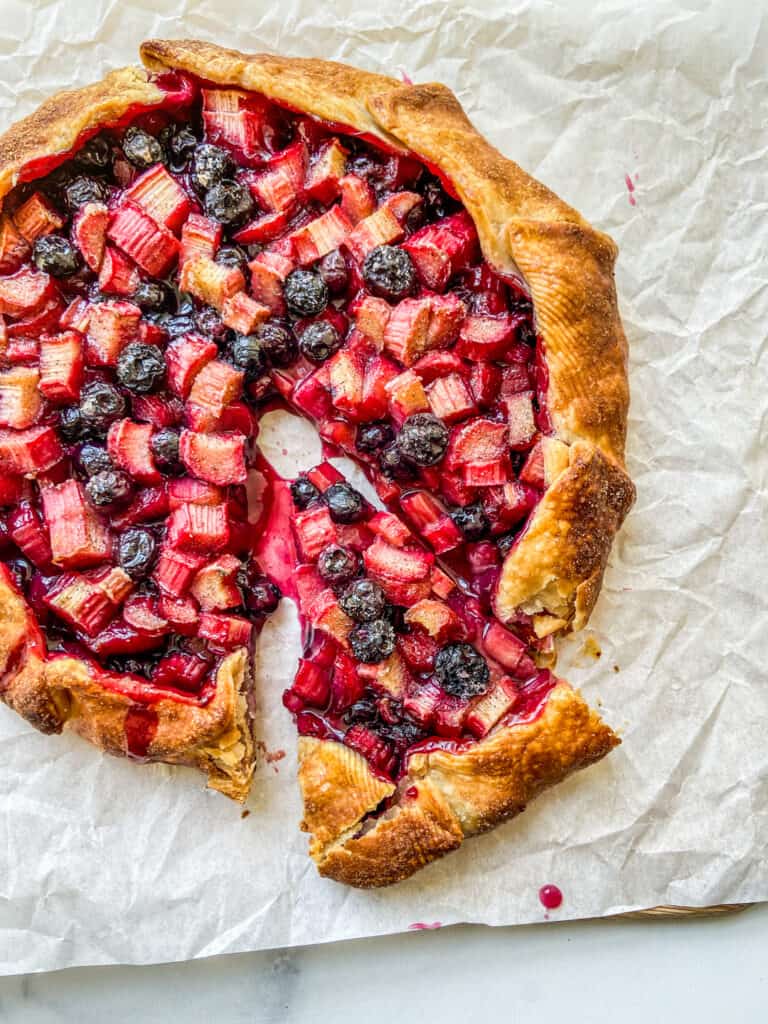 A rhubarb blueberry galette with a piece cut from it.