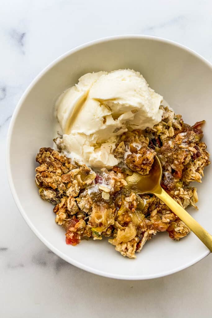 A bowl of rhubarb crisp with a scoop of vanilla ice cream.