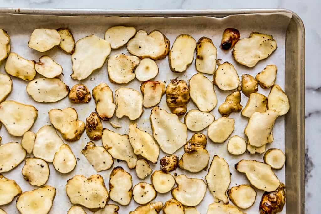 A parchment lined baking sheet with sliced sunchokes.