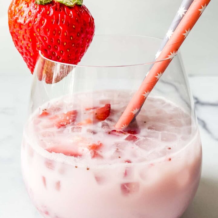 A wine glass with strawberry milk, two straws, and a whole strawberry garnish.