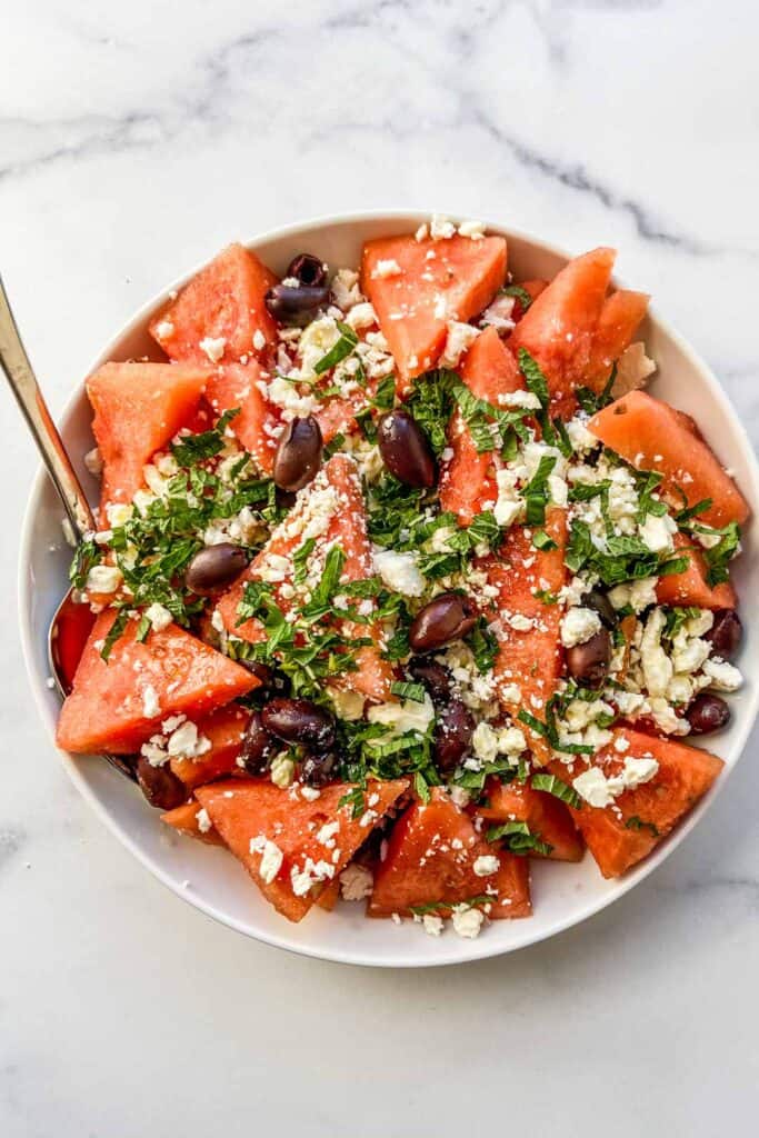 A bowl of watermelon olive salad with a large serving spoon.