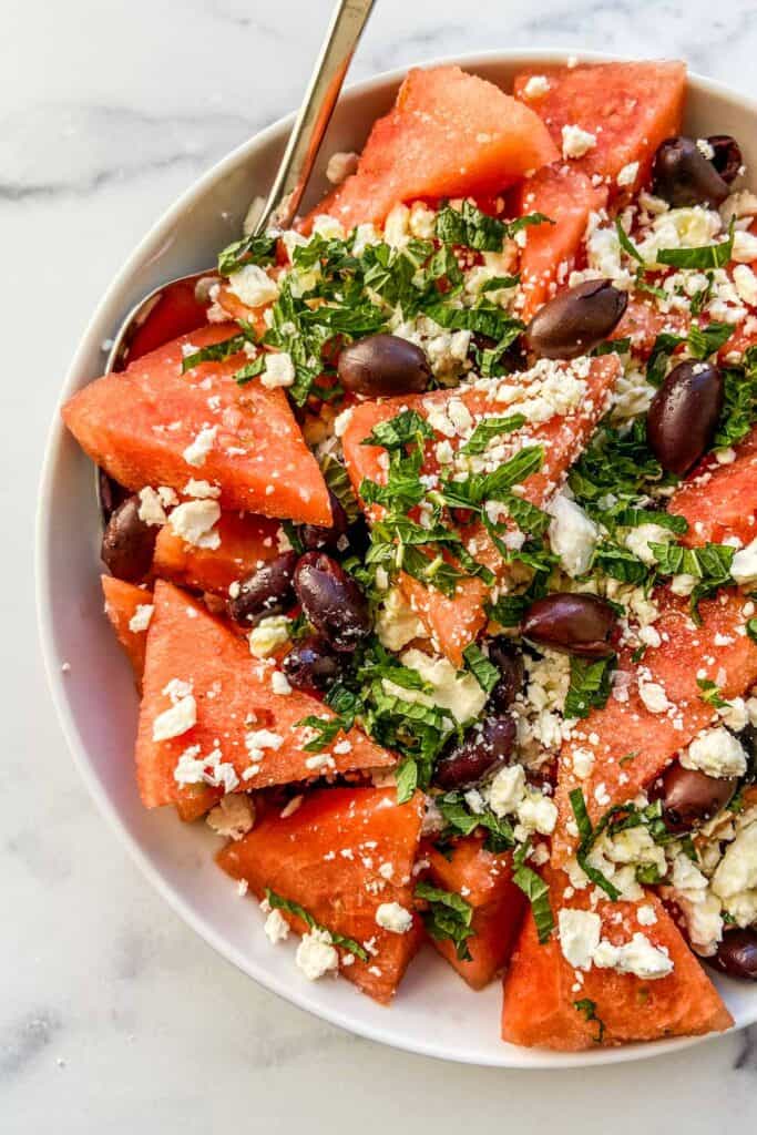 An overhead shot of a watermelon olive salad in a white serving bowl.