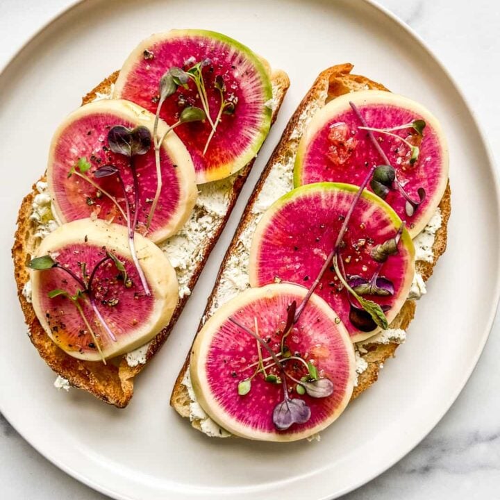 Two slices of toast with goat cheese and watermelon radish on a white plate.