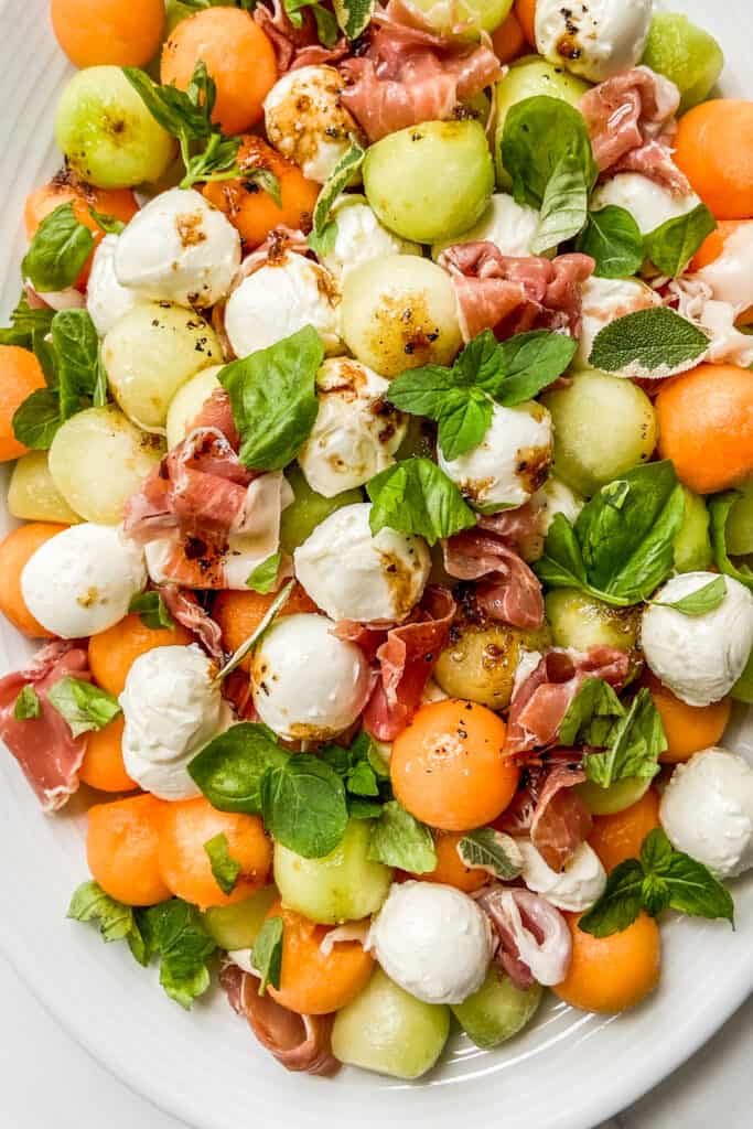 A closeup shot of a melon prosciutto salad on a white serving dish.