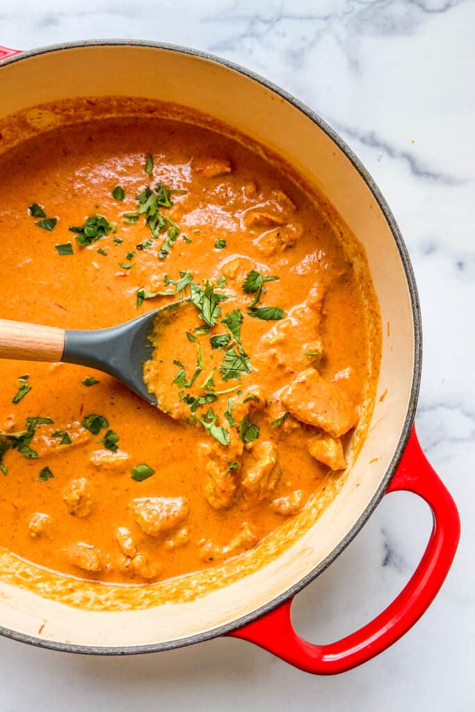 A red dutch oven with chicken tikka masala in it.