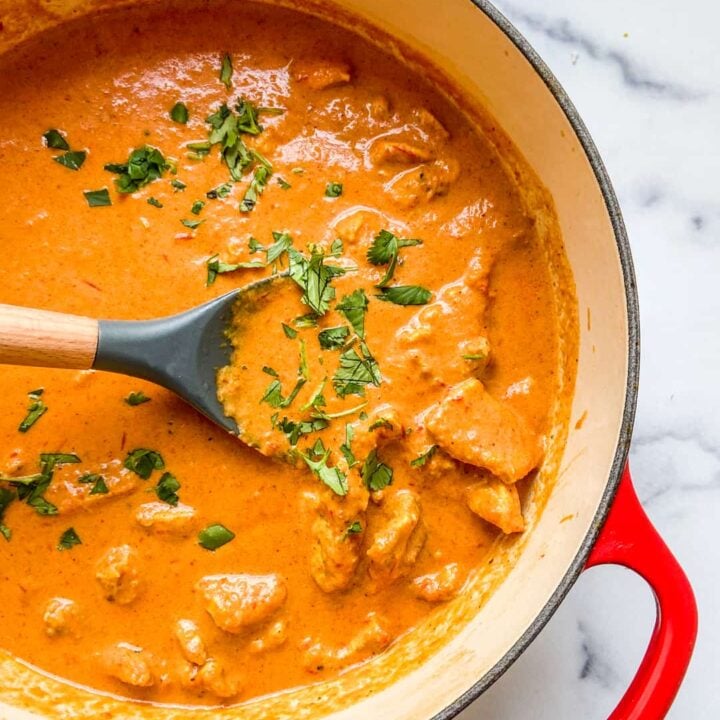 A red dutch oven with chicken tikka masala in it.