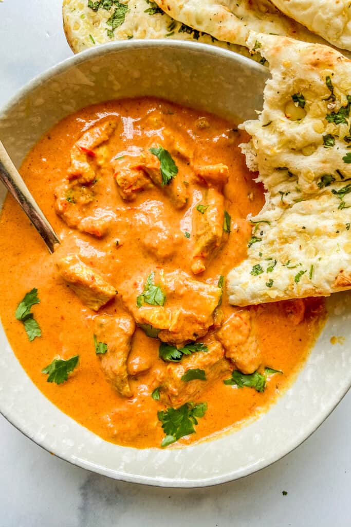 A bowl of chicken tikka masala next to some naan.