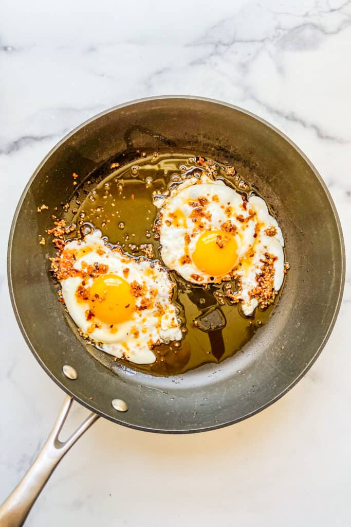 A frying pan with two fried eggs in chili crunch oil. 