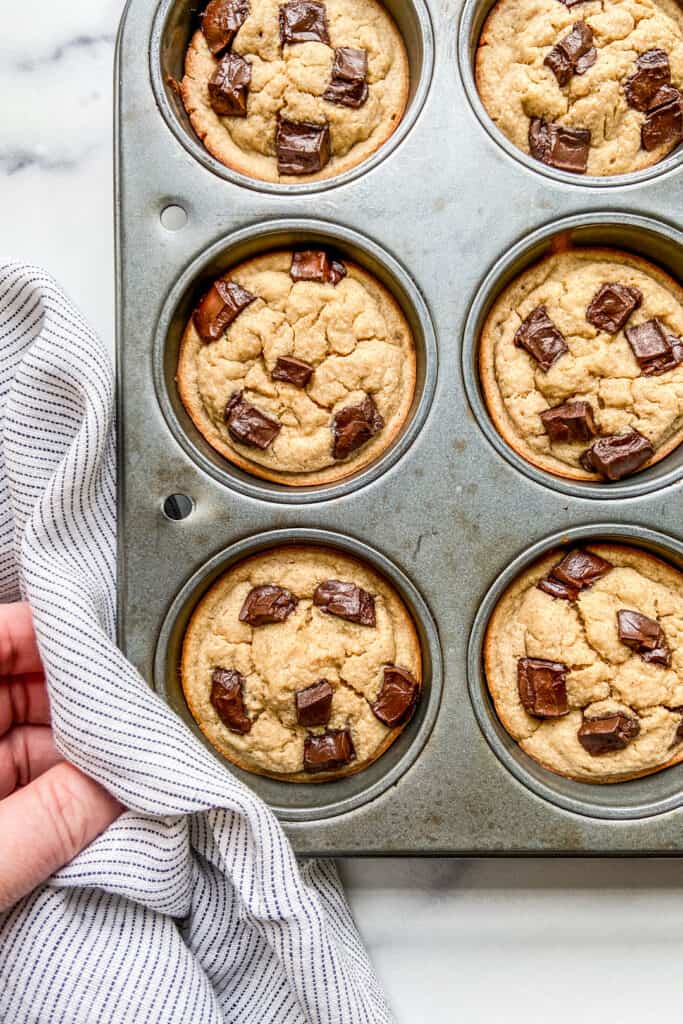 A muffin tray with baked banana muffins topped with chocolate chunks.