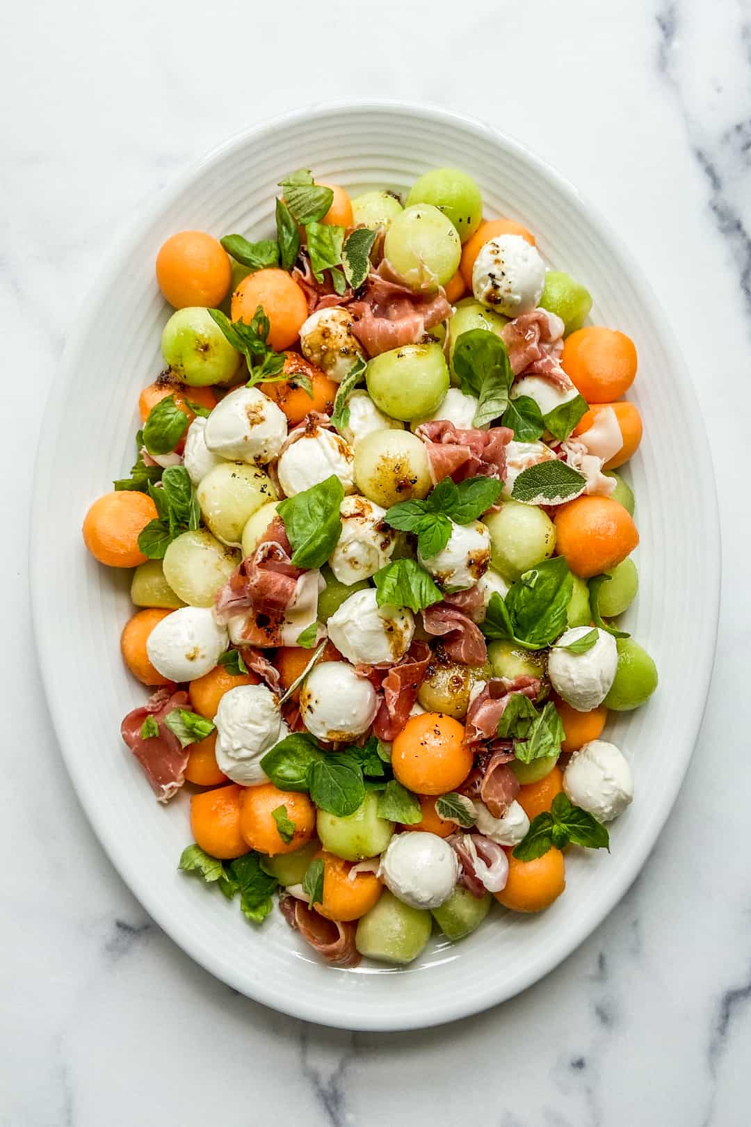 Melon prosciutto salad on a white platter.