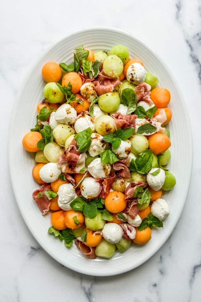 An overhead shot of an oval plate of melon prosciutto salad.