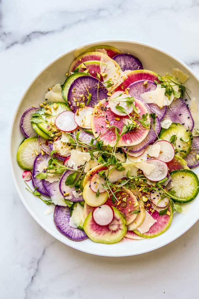 A large salad bowl with sliced radishes, parmesan, and micro greens.