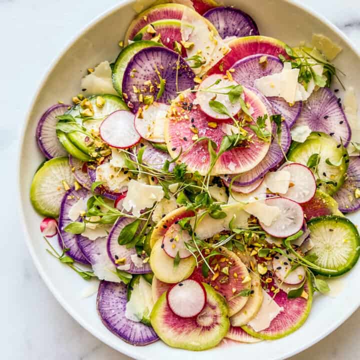 A large salad bowl with sliced radishes, parmesan, and micro greens.