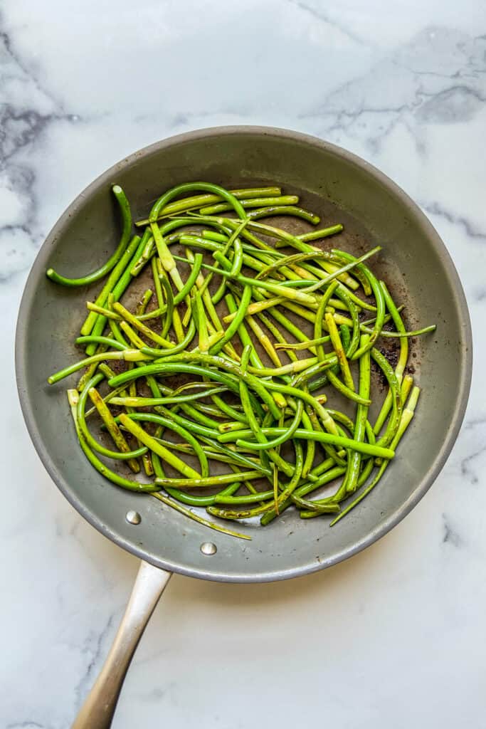 Cooked garlic scapes in a frying pan.