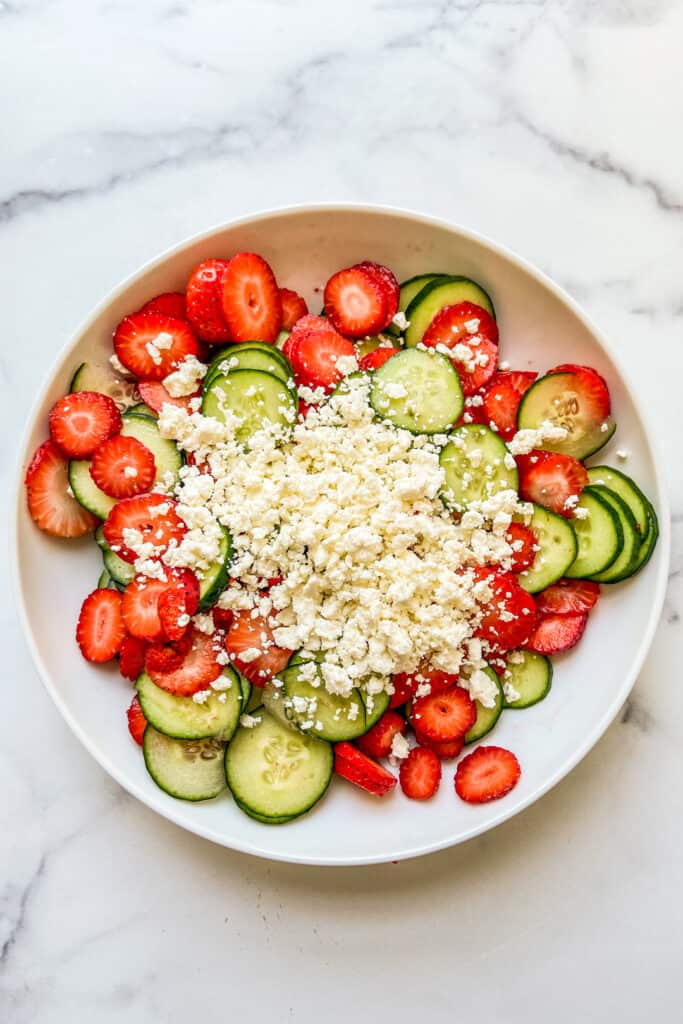 Sliced strawberries, cucumbers, and feta in a white bowl.