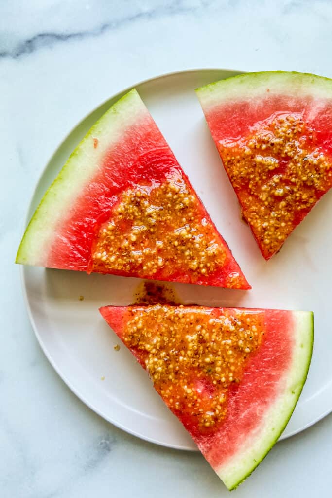 Three pieces of watermelon with mustard sauce on a white plate.