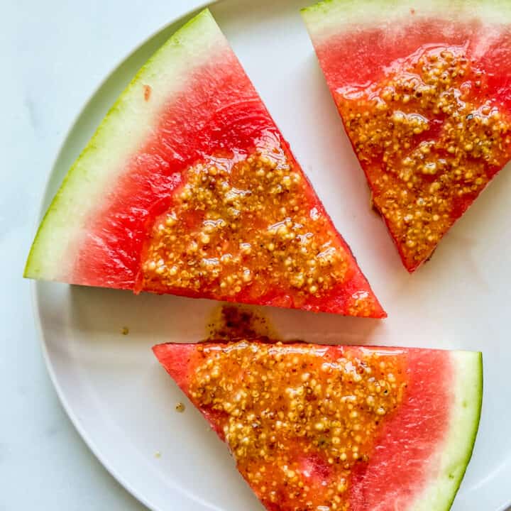 Three pieces of watermelon with mustard sauce on a white plate.