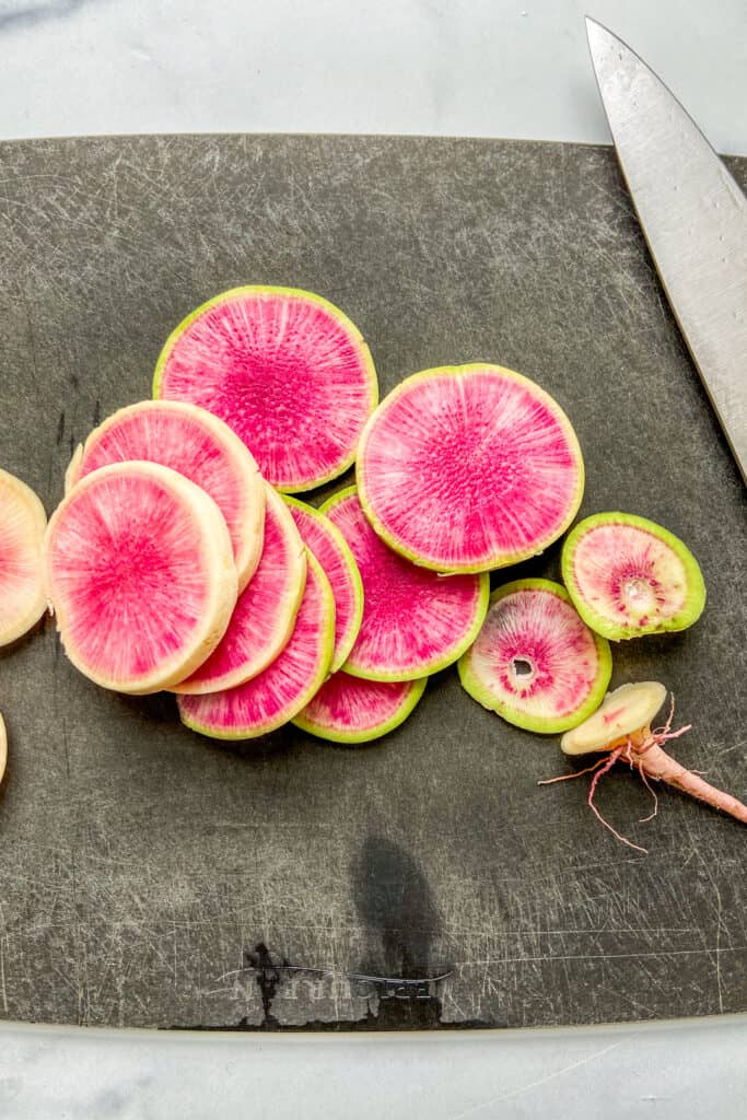 Slices of watermelon radish on a black cutting board.