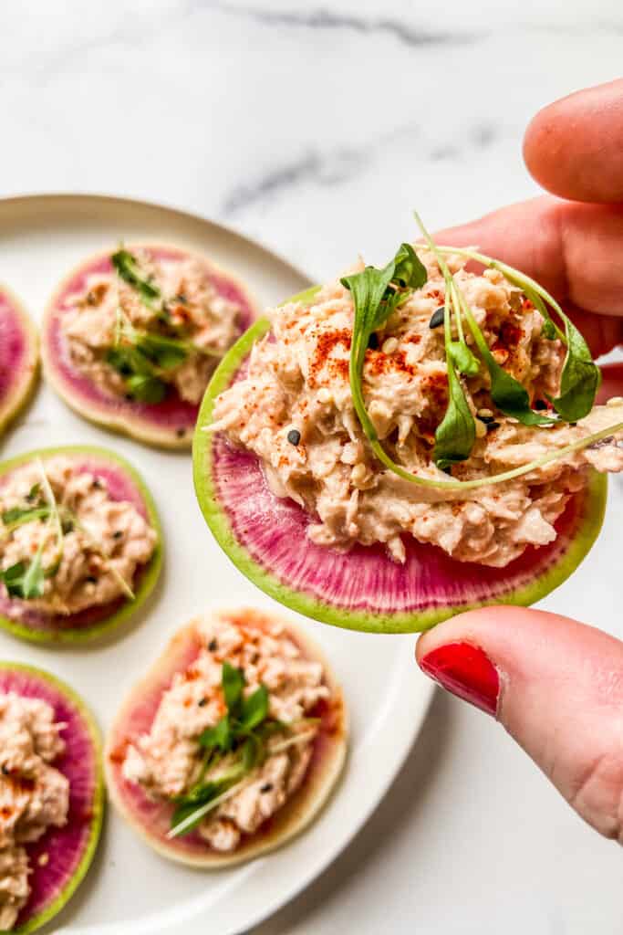 A hand holding a radish and tuna appetizer bite.