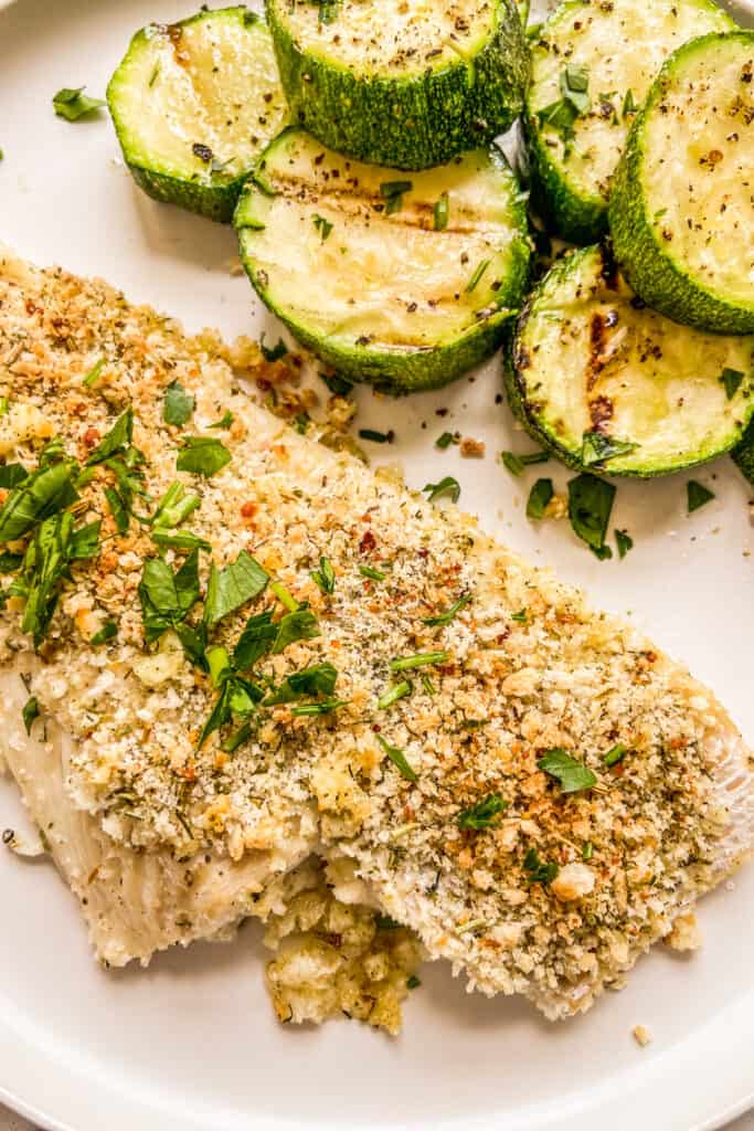 A closeup shot of crispy haddock fillets next to grilled zucchini.