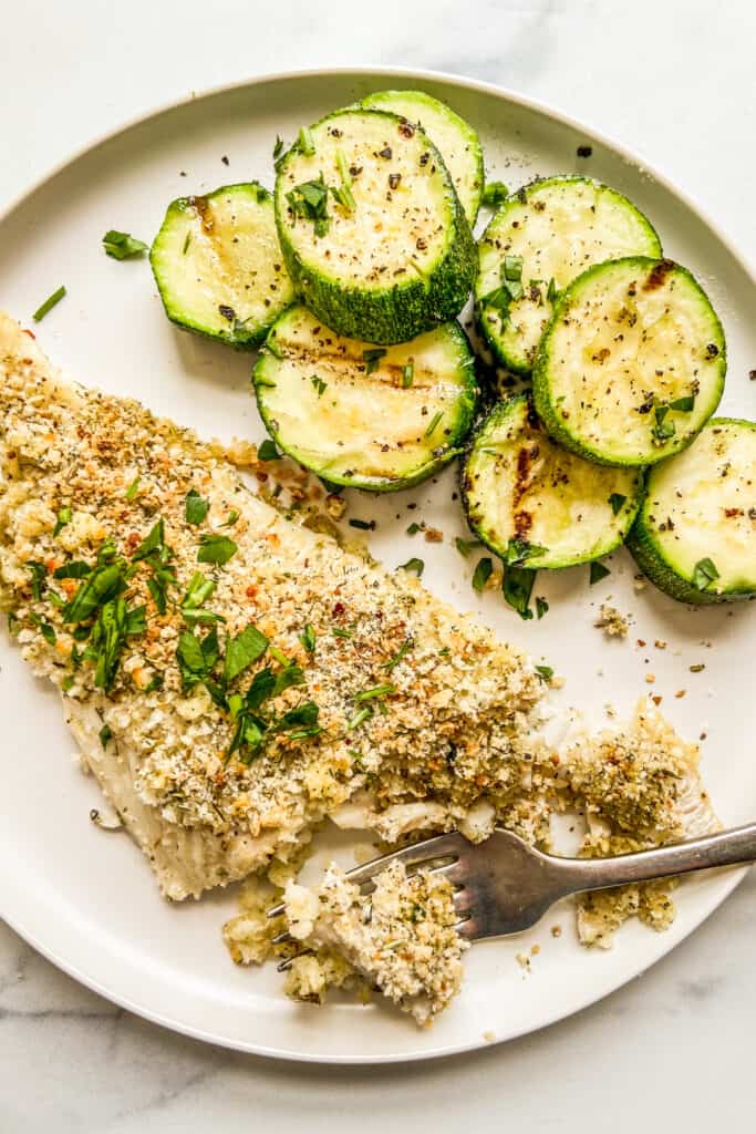 A baked haddock fillet next to zucchini on a white plate.