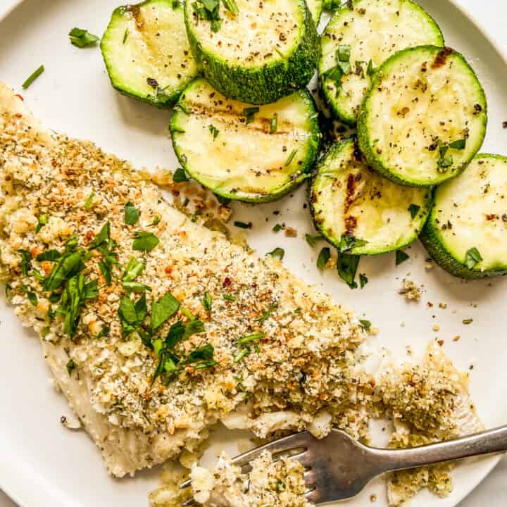 A baked haddock fillet next to zucchini on a white plate.