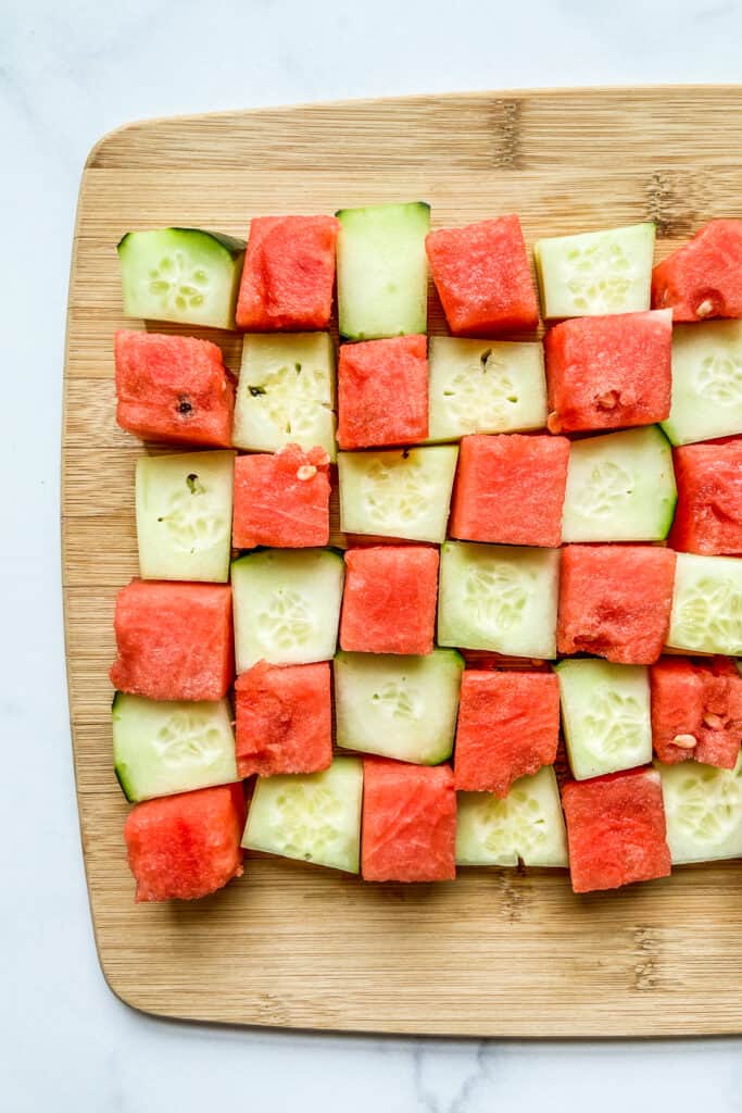 Chunks of cucumber and watermelon on a cutting board.