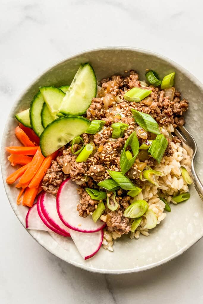 Ground beef bulgogi with rice in a bowl, topped with carrots, cucumber, and radishes.