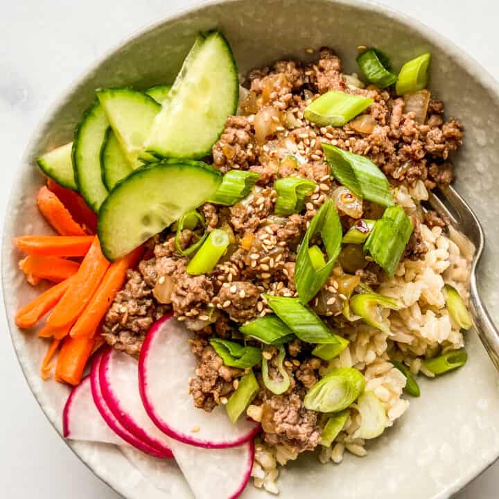 Ground beef bulgogi with rice in a bowl, topped with carrots, cucumber, and radishes.