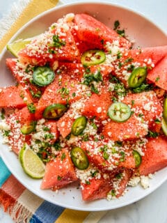 Mexican watermelon salad in a white bowl on top of a colorful napkin.